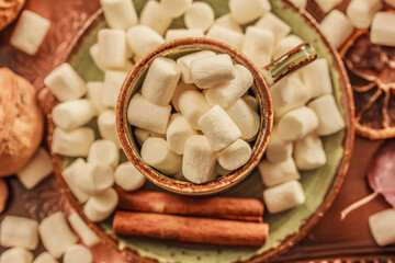 Fototapeta na wymiar A mug , cup with marshmallows, cinnamon sticks, dried orange on brown background. Cozy drink, cup coffee or hot chocolate , flat lay , close up