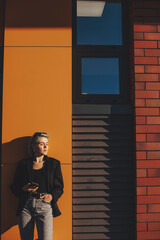 Fototapeta premium Front view of a caucasian businesswoman with eyes closed holding a mobile phone while leaning on yellow wall. Copy space. Building architecture