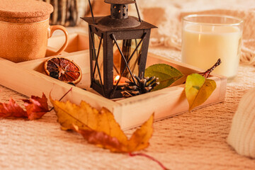 Lantern with candle, candle in a glass, mug, autumn leaves, dry orange on wooden tray on beige soft background.  Life home decor in a cozy house