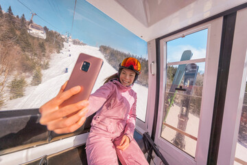 Ski vacation - Woman skier in ski lift gondola doing selfie photo or video using phone. Ski winter holidays concept. Skiing on snow slopes in mountains. People having fun on snowy day. Winter sport © Maridav