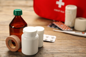 Medicaments and sticking plaster roll on wooden table, space for text. First aid kit
