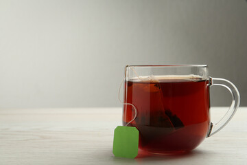 Tea bag in glass cup of hot water on white wooden table. Space for text