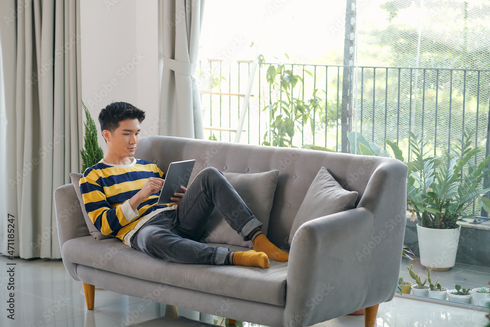 Poster man using digital tablet on sofa at home.