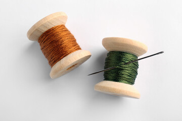 Colorful sewing threads with needle on white background, top view