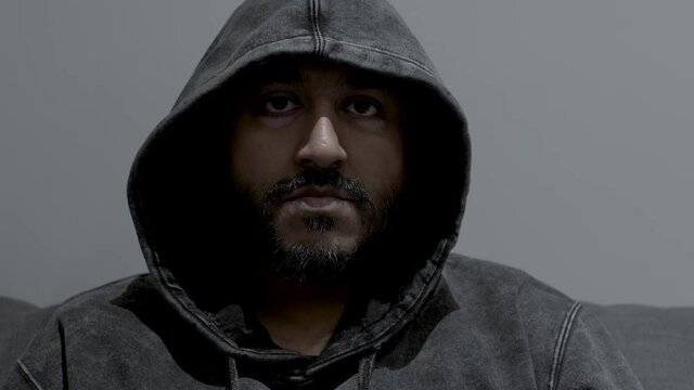 Close up dolly shot of the face of an Indian man wearing a hoodie, his eyes fixed in an intense determined stare while remaining completely motionless