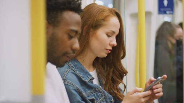 Young couple of vloggers or social influencers travelling through city on subway train for social media looking at mobile phone - shot in slow motion