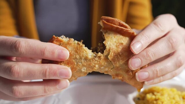 This video shows anonymous hands tearing a hot beef empanada in half, close up as it steams.
