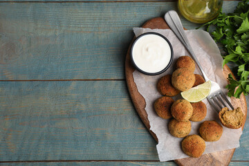 Delicious falafel balls with lime and sauce on light blue wooden table, flat lay. Space for text