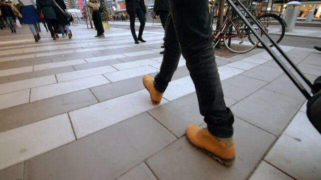 Boots of a traveller with a suitcase walking down the street in a christmas setting with christmas tree in the background