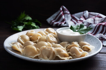 Traditional pelmeni, ravioli, dumplings filled with meat on plate, russian kitchen. Wooden rustic background, copy space.