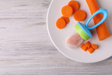 Nibbler with boiled carrot on white wooden table, top view. Space for text