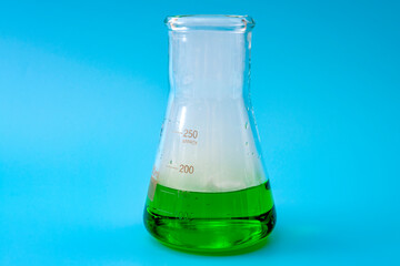 Laboratory research, smoky pharmaceutical and scientific lab test concept with Erlenmeyer flask filled with green liquid and realistic smoke coming out of it isolated on blue background