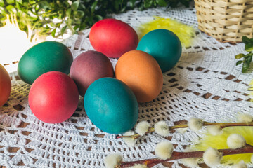 Fototapeta na wymiar Colorful Easter eggs on a handmade crocheted tablecloth or hand knitted wool napkin. Rustic Easter composition, with boxwood and pussy willow branches.