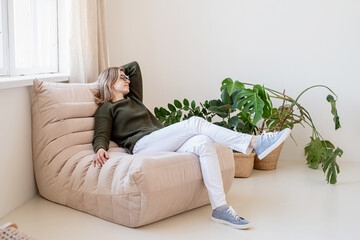 Obraz premium Attractive young woman sitting on the chair in light and airy interior with plants
