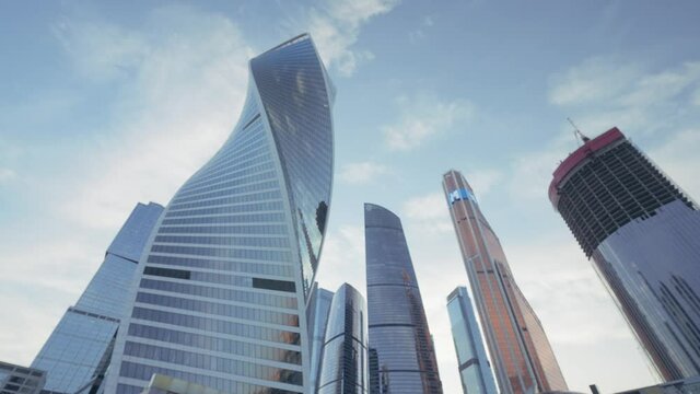Bottom view of a twisted skyscraper on blue cloudy sky background. Action. Glass facade tall buildings in the business city center.