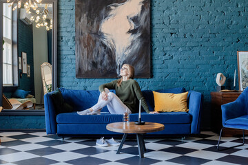 Obraz premium Young woman sitting on coach in stylish living room