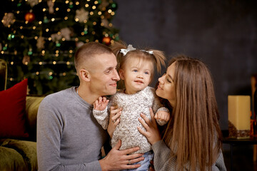Joyful happy family with little baby girl in aesthetic cozy home interior near festive Christmas tree. Beautiful couple in love. Good mood and having fun together. Merry Christmas. Happy parenthood