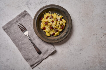 Traditional Mediterranean potato gnocchi with parmesan and dried tomatoes in dark plate, with fork on linen napkin. Top view. Copy space