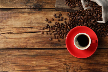 Cup of aromatic coffee and beans on wooden table, flat lay. Space for text