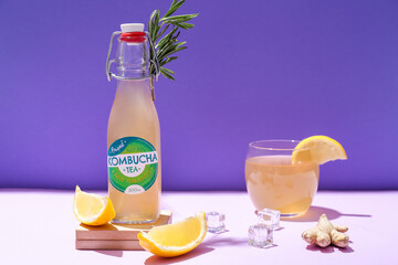 Bottle and glass of natural kombucha on purple background
