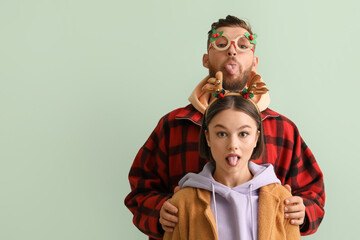 Grimacing young couple in stylish winter clothes and with Christmas decor on light background