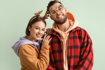 Happy young couple in stylish winter clothes and with Christmas decor on light background
