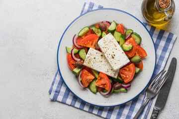 Traditional Greek rustic salad with tomatoes, cucumbers, onions, feta cheese, olive oil and herbs in plate on light background, top view