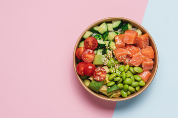 Salmon, avocado, cucumber, tomato, edamame beans and rice poke bowl on pink blue background