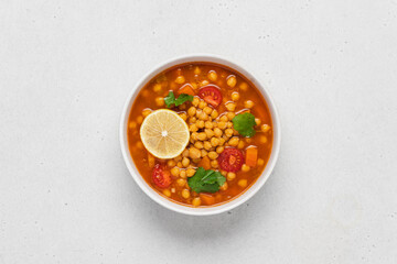 Chickpea lentil soup with vegetables, cilantro and lemon in light bowl on white table. Vegetarian soup top view