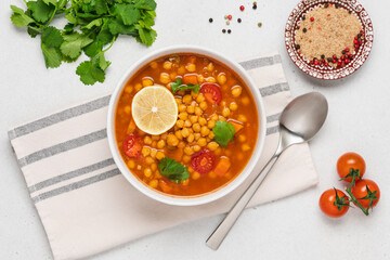 Chickpea lentil soup with vegetables, cilantro and lemon in light bowl on white table. Vegetarian soup top view