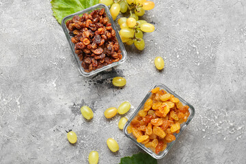 Glass bowls with tasty raisins and ripe grapes on grey background