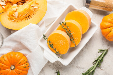 Baking dish with fresh pumpkin pieces on light background
