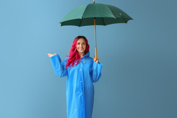 Beautiful woman in raincoat and with umbrella on color background