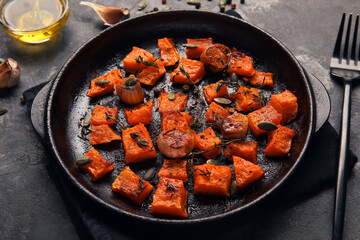 Frying pan with tasty roasted pumpkin on black background