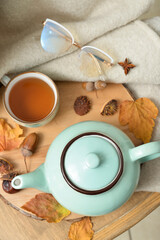 Tea pot, cup of hot beverage, eyeglasses and autumn leaves on table in room