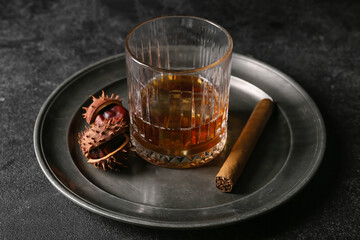 Glass of cold chestnut whiskey and cigar on black background