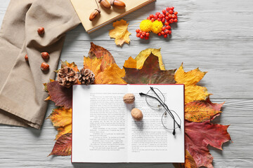 Composition with open book, eyeglasses and beautiful autumn decor on light wooden background