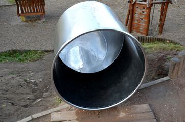 stainless steel slide on the field with grassy hills and wooden palisades. Large glossy tube for sliding children with an impact on the tartan rubber pad. the end of the tube is an open trough