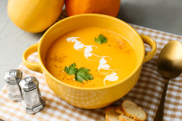 Pot with delicious pumpkin cream soup and spices on table, closeup
