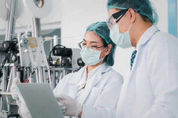 Both male and female Asian scientists are outfitted with protective gear. Examining the factory's machinery and materials used in the mask-making process. Covid 19 is a piece of preventive equipment.