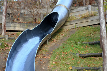 stainless steel slide on the field with grassy hills and wooden palisades. Large glossy tube for...