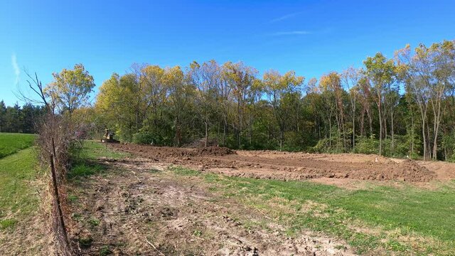 Wide angle view of a yellow bulldozer leveling soil at a construction site with wooded area in background in early autumn; concepts of industry, construction and economic growth