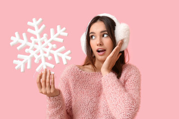 Surprised young woman in earmuffs with snowflake on pink background