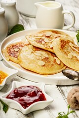 Delicious homemade pancakes with almond petals on a white plate. Tasty traditional breakfast. Pancakes with jam on a white rustic background. Serving white tableware. Sweet dessert. Vertical shot