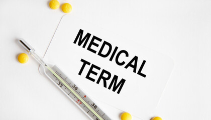 Obraz premium On the business card is the text MEDICAL TERM, next to yellow tablets and a thermometer.