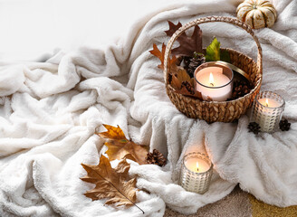 Fototapeta na wymiar Burning candles in holders and autumn decor on soft plaid in room