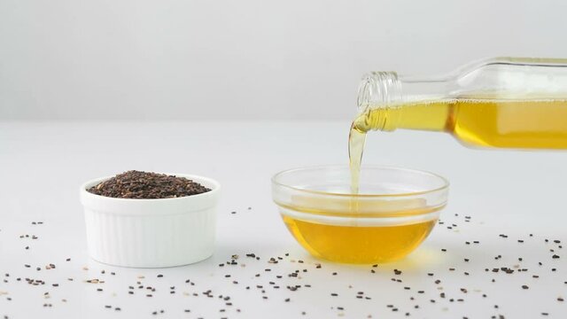 Pouring sesame oil in a cup with sesame seeds in a bowl.
