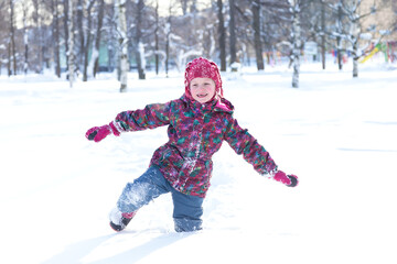 Fototapeta na wymiar Winter activities outdoors. Happy little girl wearing a warm clothes walking through the snowdrifts in snowy park on cheerful winter day