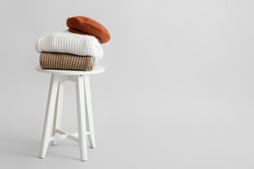 Stylish winter clothes on stool against light background