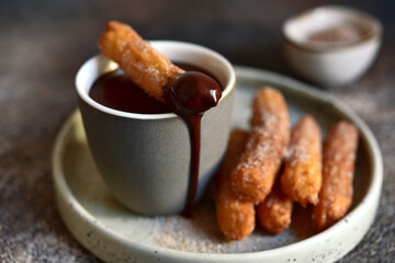 Traditional spanish dessert churros - fried choux pastry with chocolate sauce on a plate .